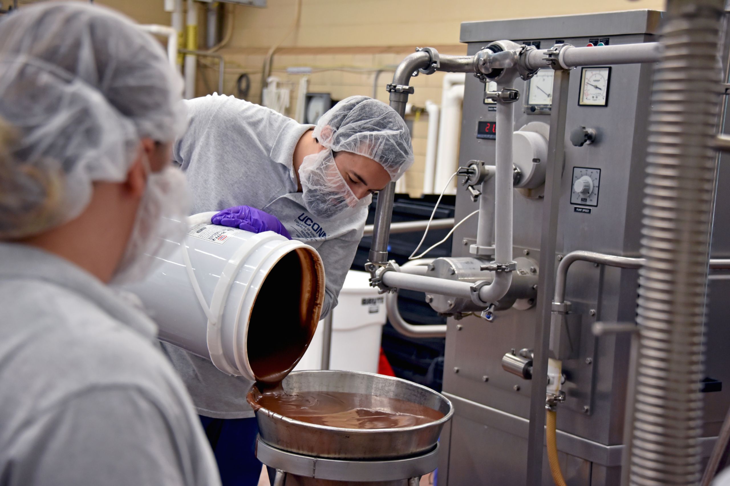 A man pouring liquid into a funnel attached to a machine inside of a plant
