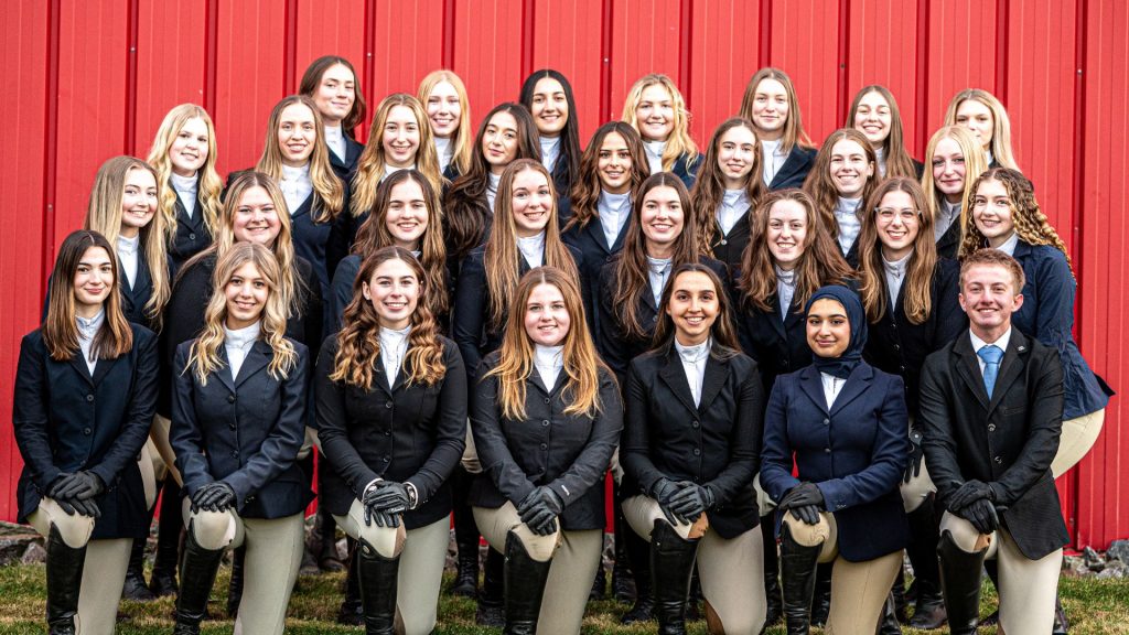The Equestrian Team posing for a group photo in front of a red barn.