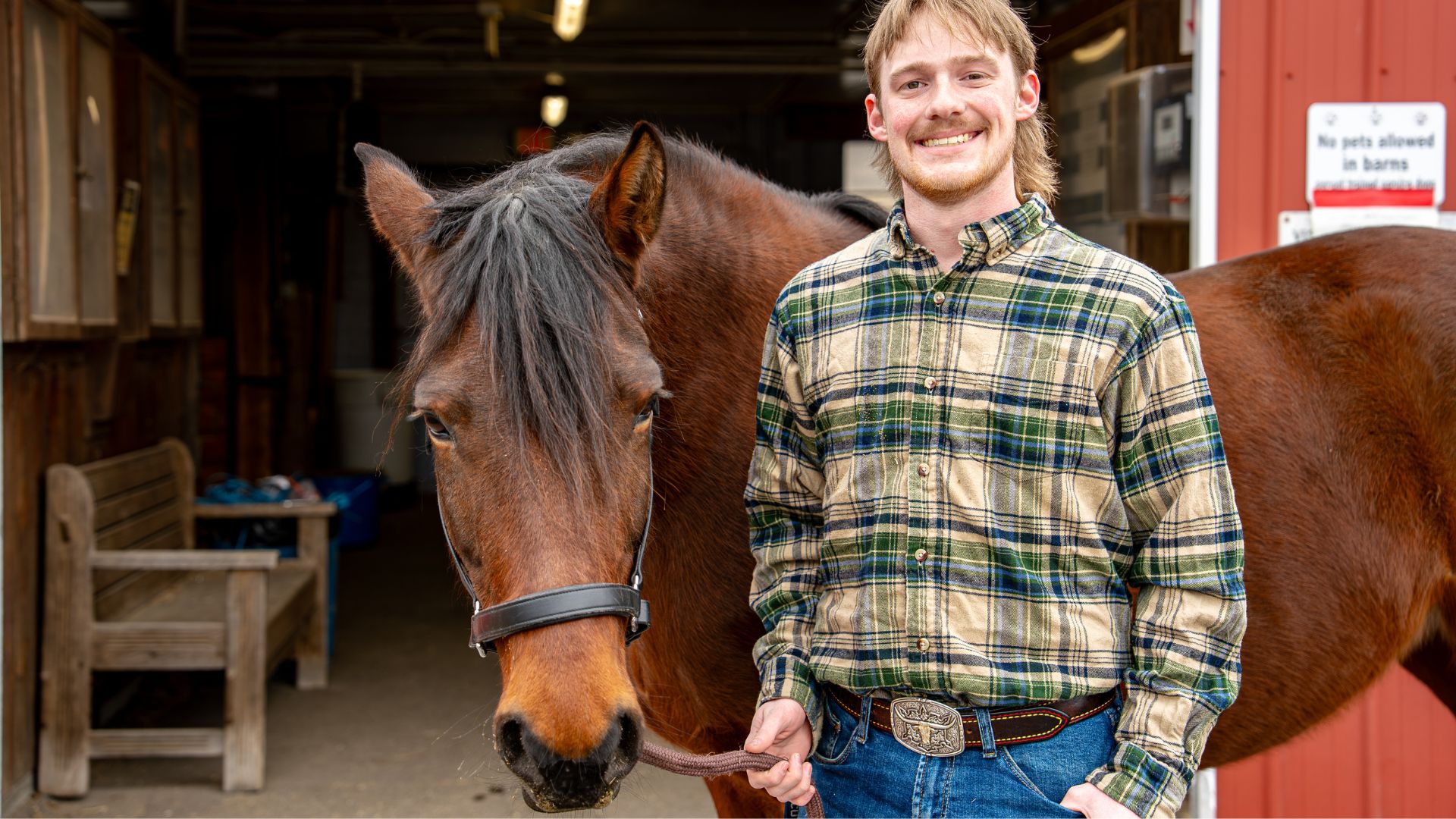 A man posing for a photo with a horse outside of a red barn